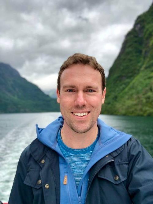 Chris Penzien on a boat with water and mountains in the background